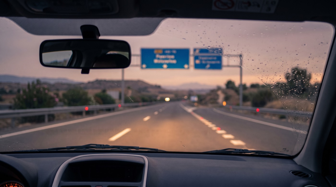Carretera al anochecer vista desde el interior de un coche con los faros encendidos